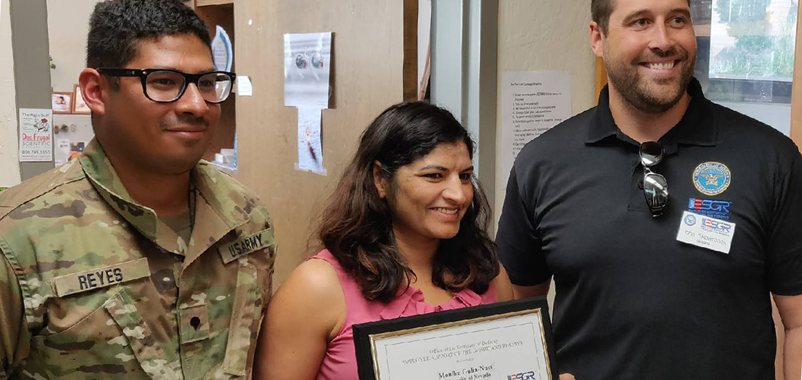 Monika Gulia-Nuss holding plaque while standing between Jeremiah Reyes on left and Johnny Skowronek on right