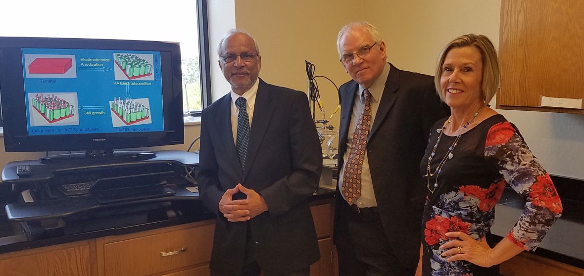 Three faculty members in business attire stand side-by-side in a computer-based laboratory.