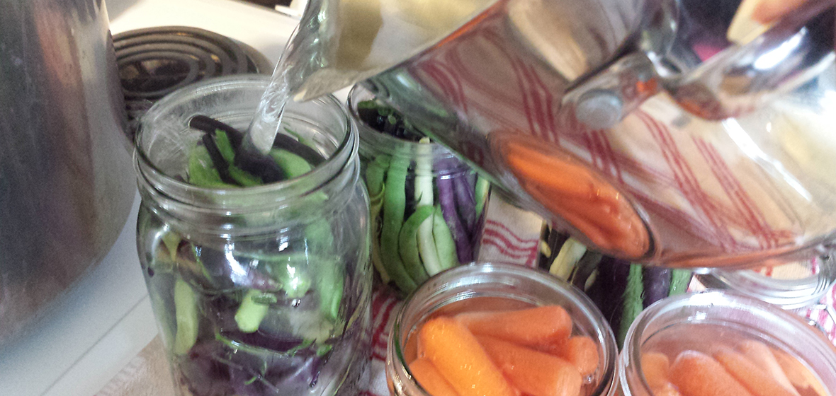 Hot water pouring into a jar of vegetables