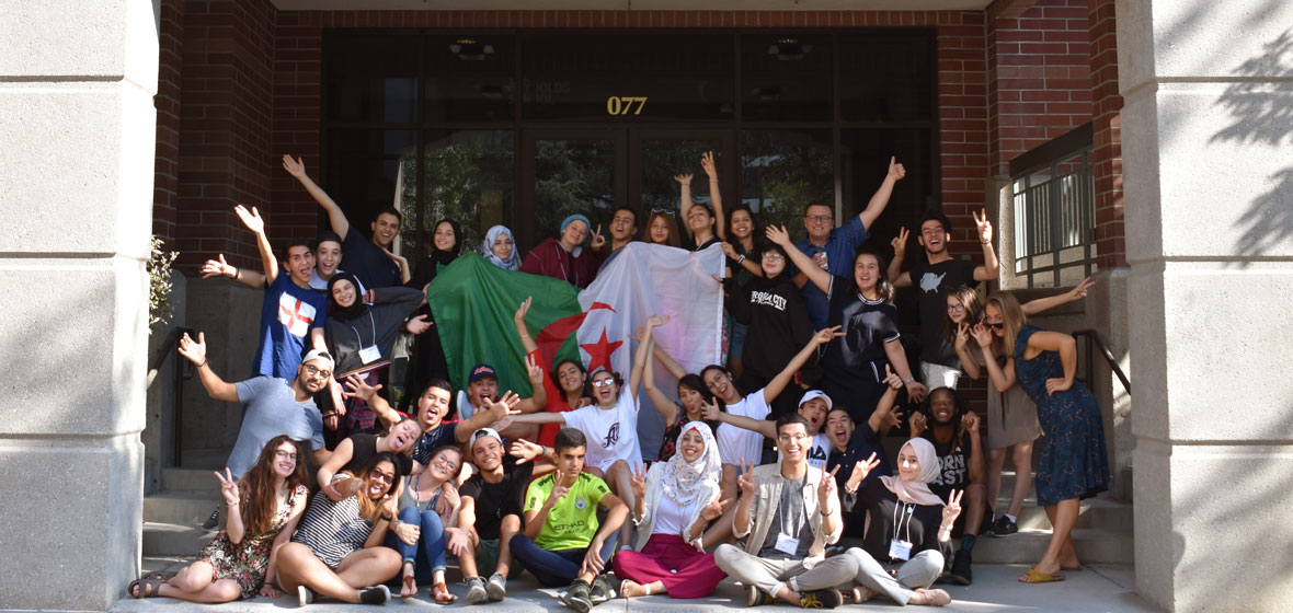 Group of students, faculty and program staff pose in front of the Reynolds School of Journalism.