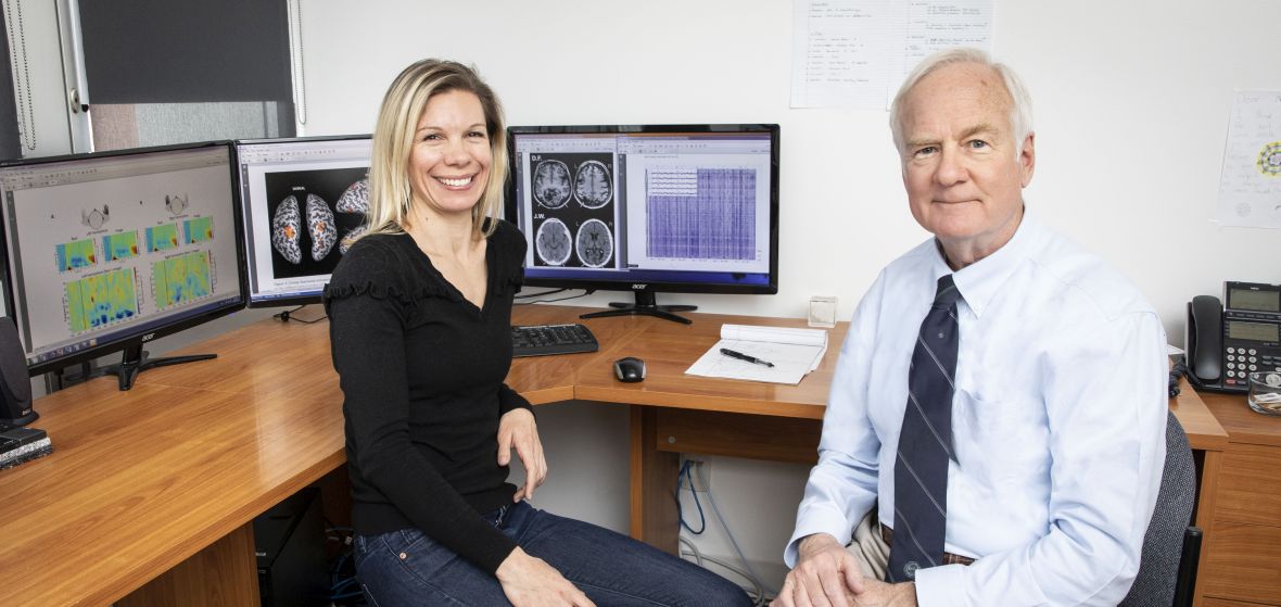 2 faculty member sitting at desk in office with neuroscience-related images on the computer screens