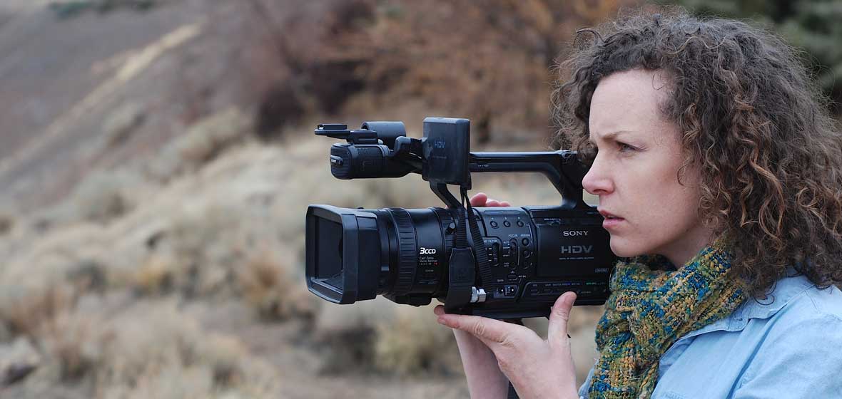 A woman points a camera at something off-screen. 
