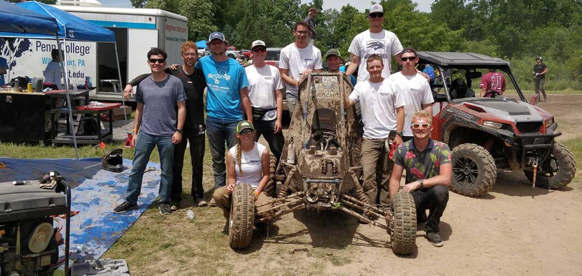 A group of students around a muddy racing car.