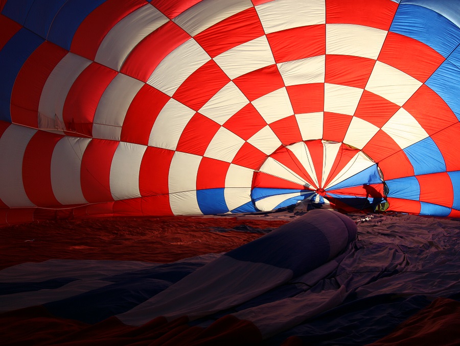 Deflated hot air balloon with red and white checkers and people's shadows in the background.