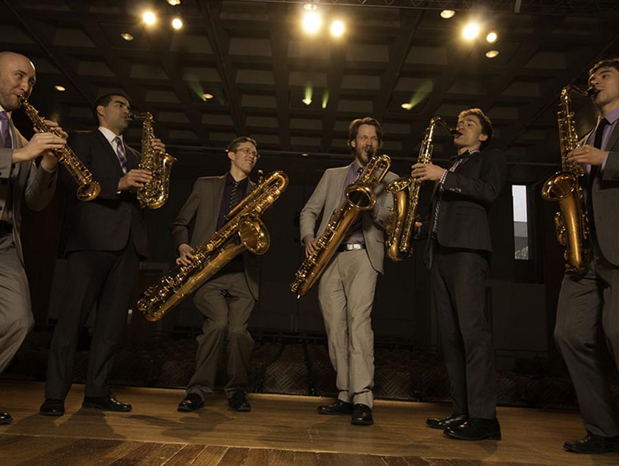 A group of musicians in suits gathered playing a variety of different saxophones