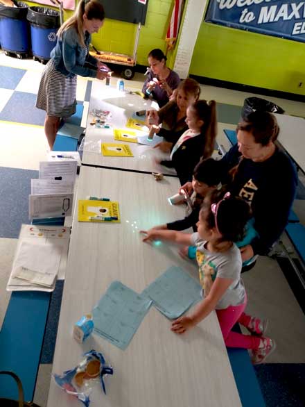 Parents and children with craft supplies sitting at a school cafeteria table