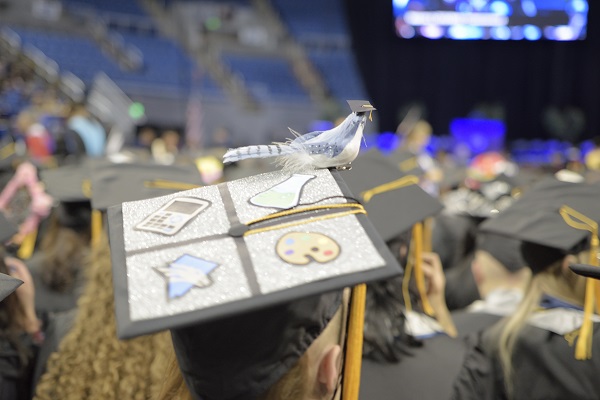 A 2019 Winter Commencement graduate with a mortar board that has a bird sitting on it with its own mortar board 