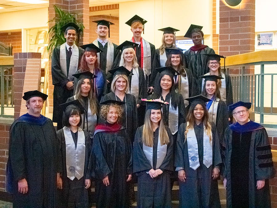 A group of students and faculty pose for a picture indoors wearing regalia.