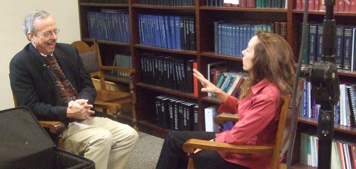 George Lewis and Valerie Fridland sitting and talking in a room with books and bookshelves behind them.