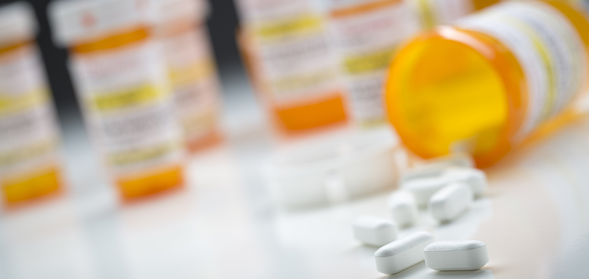 Multiple prescription bottles with one tipped over in the foreground and pills in front of it.