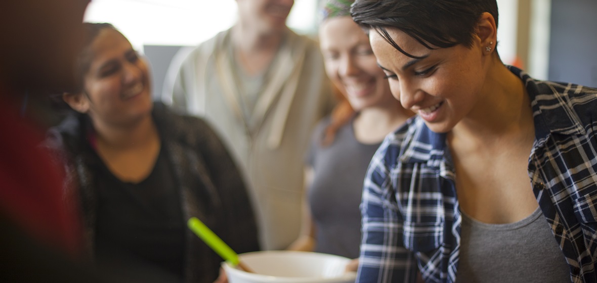 Misha Fotoohi and classmates, one with a mixing bowl, laughing while cooking