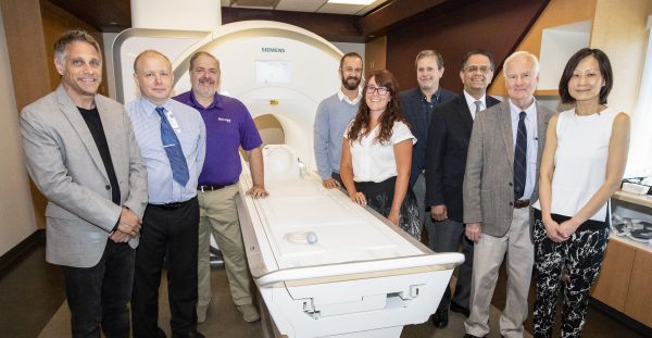 9 people pose in front of MRI machine