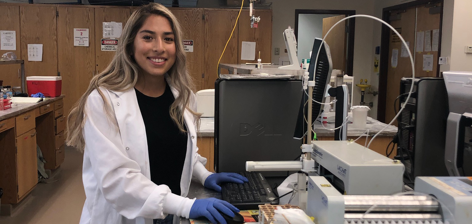 A student in a laboratory smiles for the camera. 