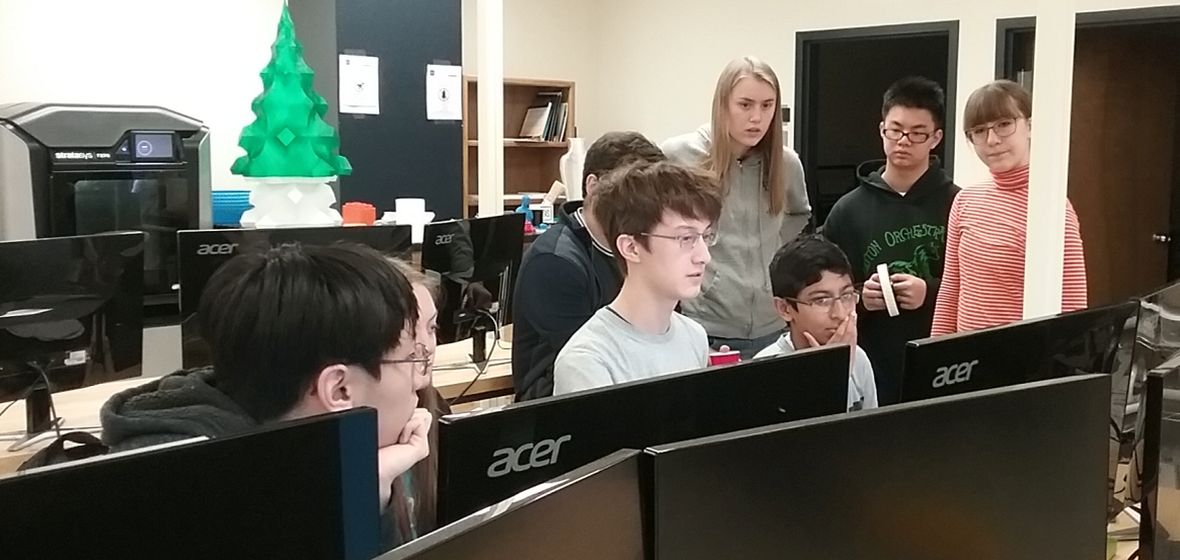 Seven high school students working at computer stations in a makerspace