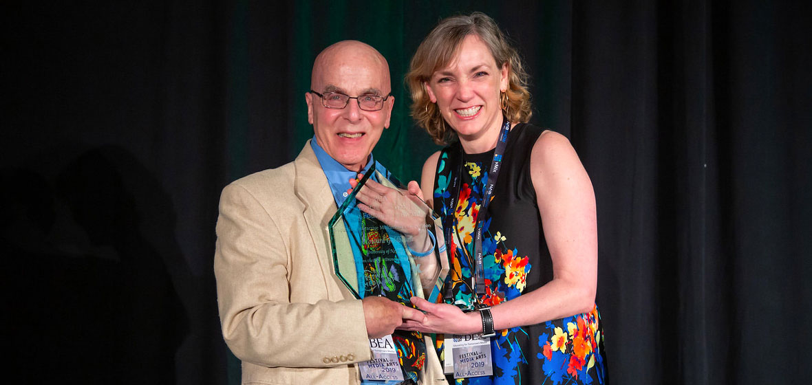 Two people pose on stage holding an award.