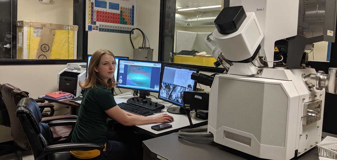 Cayla Harvey in front of a computer and large scanning microscope in a laboratory.