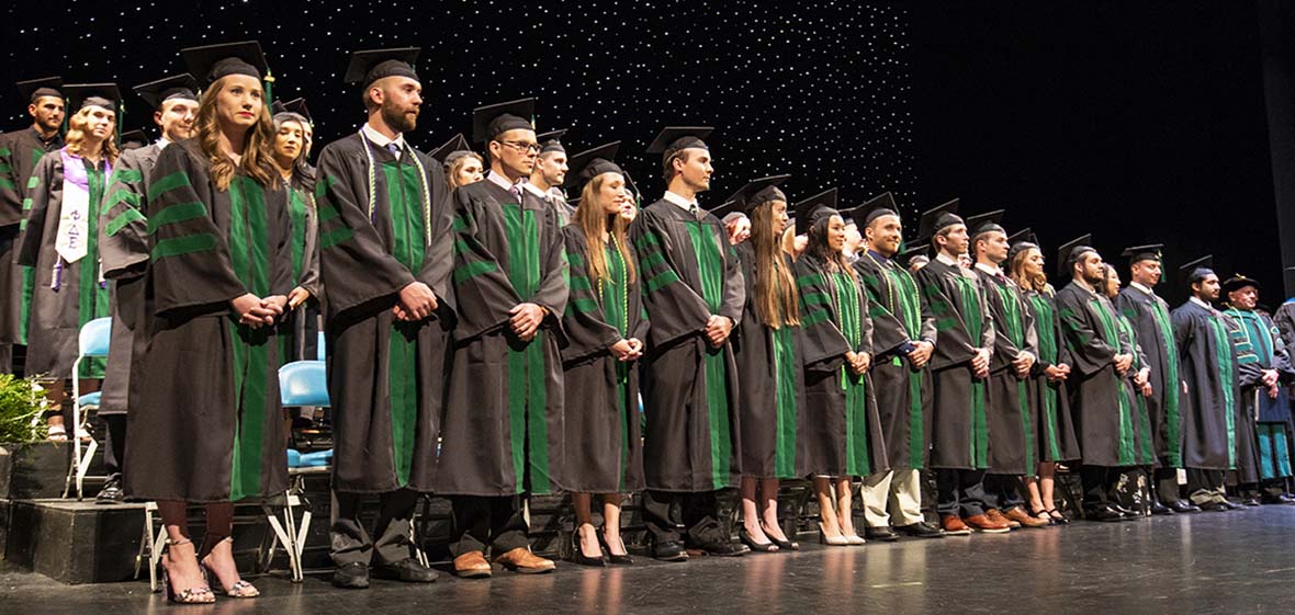Graduates in black robes and green stoles standing on a stage