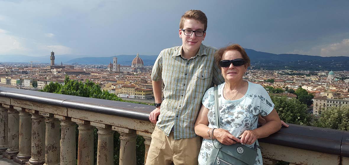 Young man and older woman pose for a photo standing by a brick railing with an Italian city landscape behind them