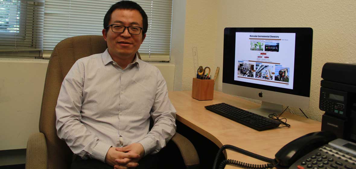 A professor sits at a desk with a computer.