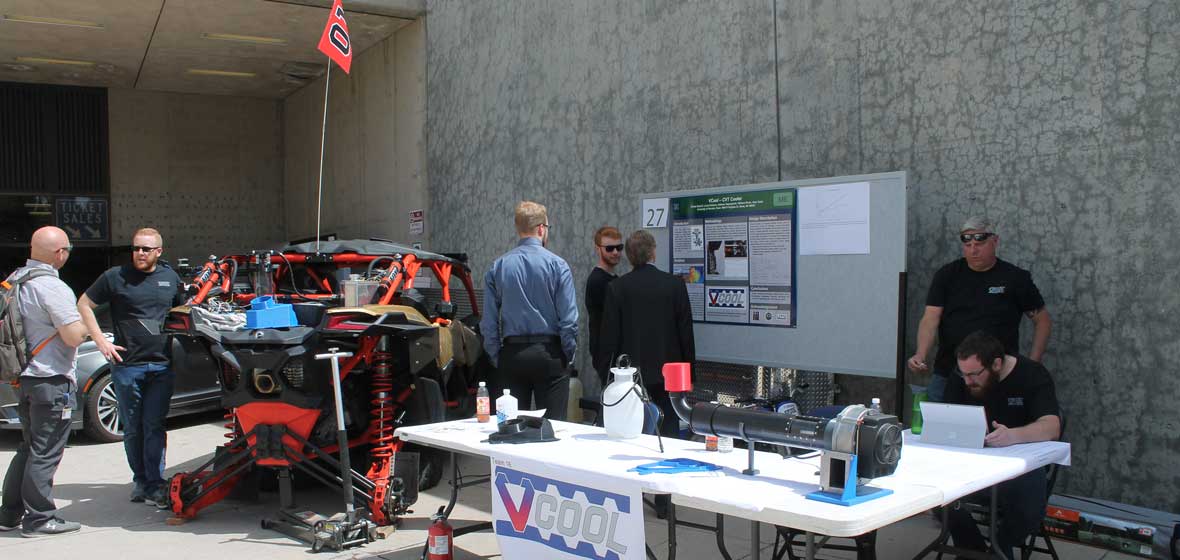 A group of students gathered around a car, discussing the project and its poster.