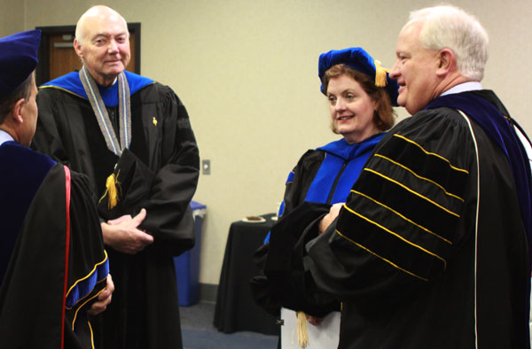 Four adults speak in a group wearing graduation attire.