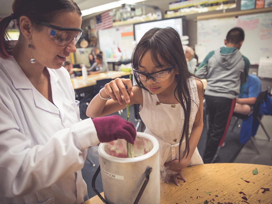Kimberly Hernandez helps a young student dip a rose into a container of liquid nitrogen.