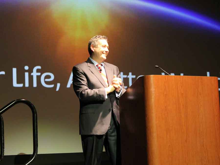 Allan Swan stands behind a podium on stage.