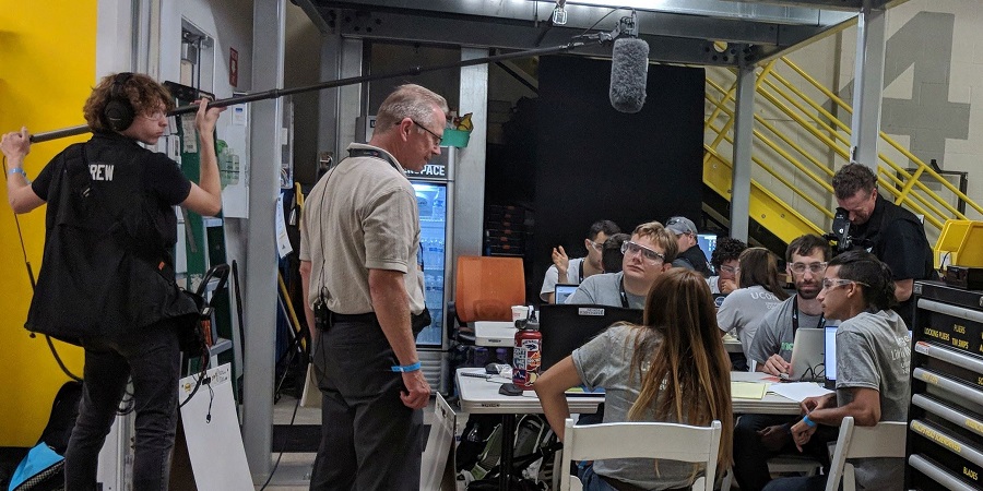 Make48 team sitting around tables on set with cameras