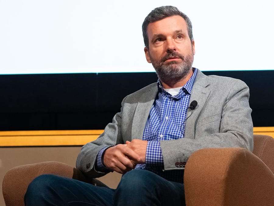 Man looks off into the distance sitting in a chair on stage.