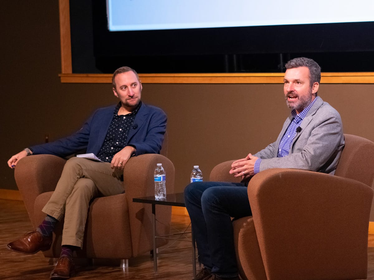 Two men sit on stage.