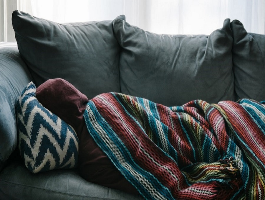 A person in a hoodie sleeping on a couch with a colorful blanket