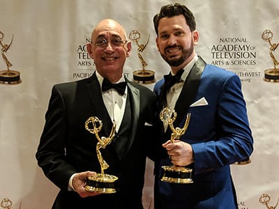 Two men pose holding Emmy Awards.