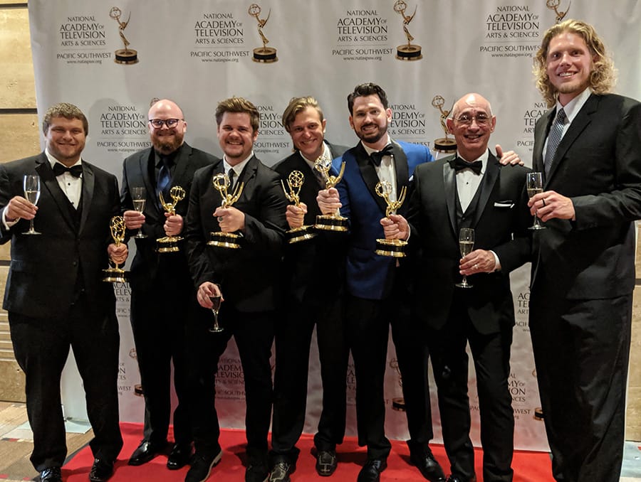 A group of men pose on a red carpet holding Emmy Awards.