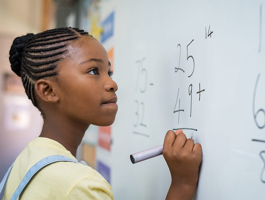 A young girl solves a math problem on a classroom's whiteboard