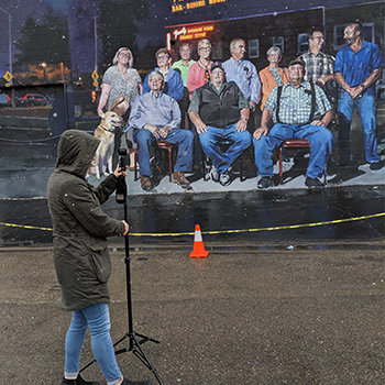 Laura Rocke sets up a VUZE camera to capture 360 video of the inaugural Elko Mural Expo. This mural is titled, "Far Westeko Euskal Herria" by Sebastian Velasco from Spain. It is located at The Star in Elko and features a portrait-style image of many different people.