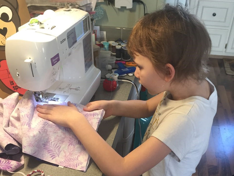 Young girl using a sewing machine to sew pink palm leaf printed cloth