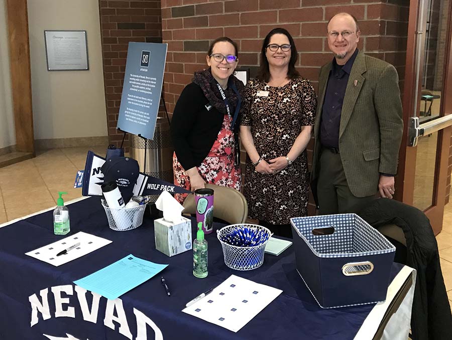 Lexi Erwin, Chai Cook and Brian Frost stand behind a check-in table at the Administrative Faculty Committee Brown Bag Panel event March 10, 2020.