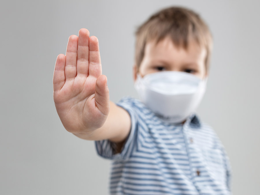 Child wearing a mask with hand up gesturing stop