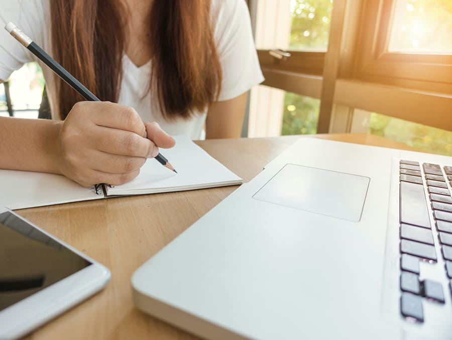 Student writes notes in front of their laptop and phone.