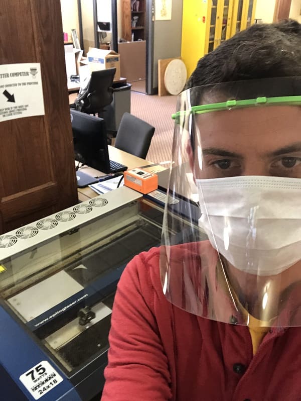 Nick Crowl dons a face shield made in the DeLaMare Library as he operates a 3D printer.