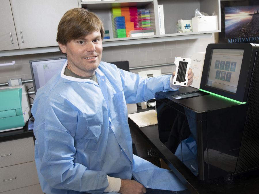 Dr. Paul Hartley sits at genomics sequencing machine in laboratory