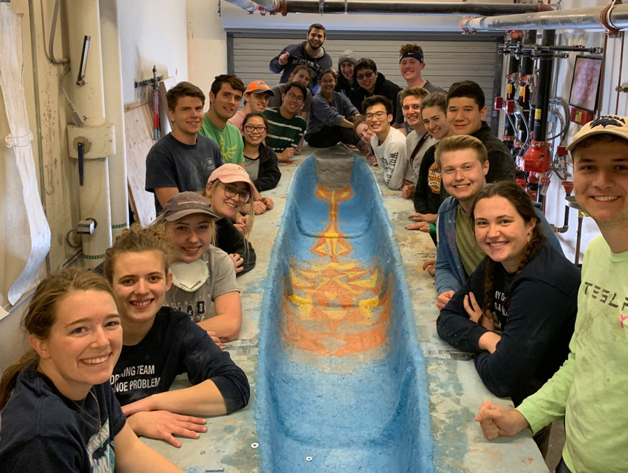 A group of students surrounds the canoe that they built. 