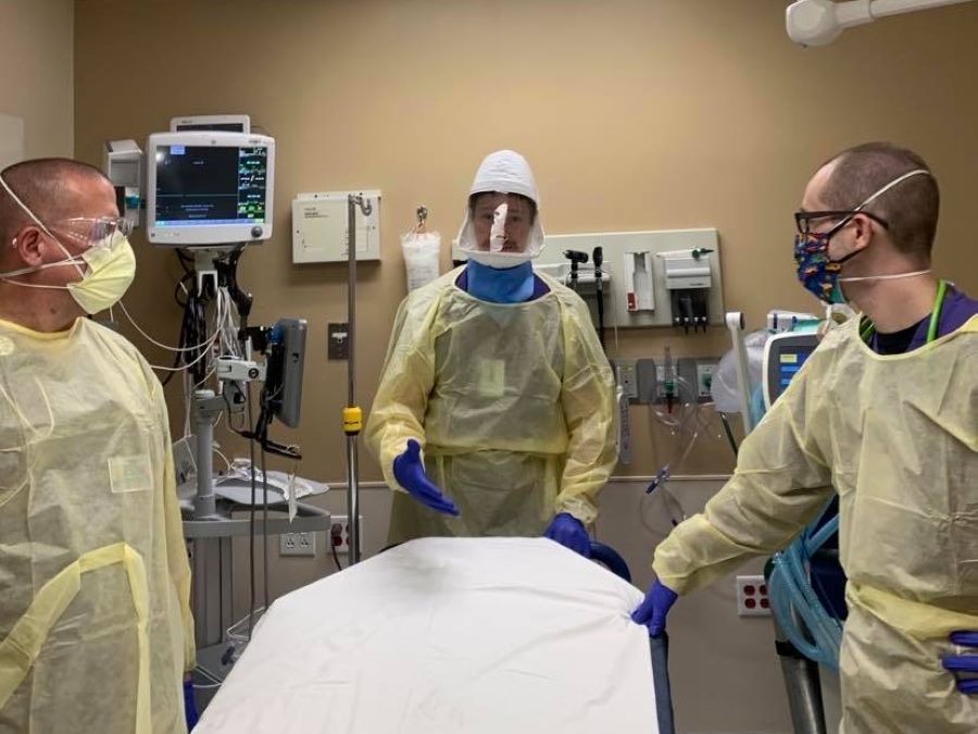 Three healthcare workers wearing protective gear including masks, shields and gowns, in a procedure room.