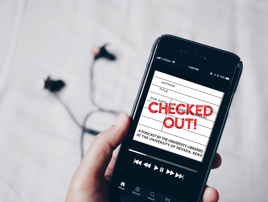 Unidentified person holds a smartphone with headphones in the background. On the screen of the smartphone is an image of the “Checked Out!” podcast art. It features a white background and looks like an old fashioned library check out card. There is a red stamp across the image that says “Checked Out!” “Checked Out!” is a podcast by the University Libraries at the University of Nevada, Reno.