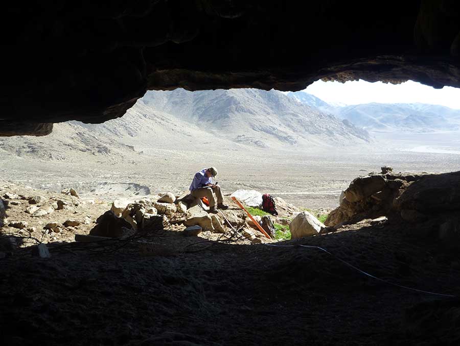 A man sits in the opening of a cave overlooking the Nevada dessert