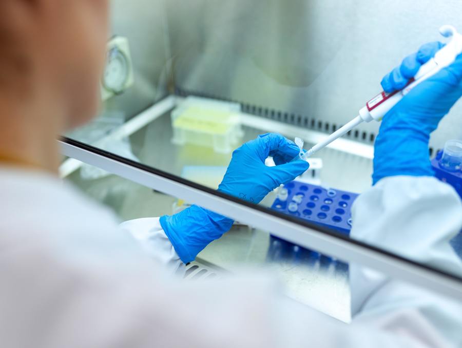 Lab technician's gloved hands holds an instrument putting a chemical substance into a vial.