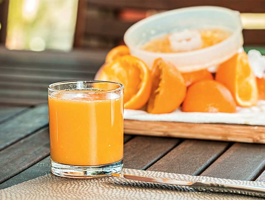 A glass of fresh-squeezed orange juice on a table next to fresh orange slices