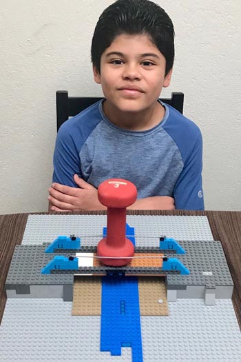 boy showing bridge made of Legos supporting a hand weight