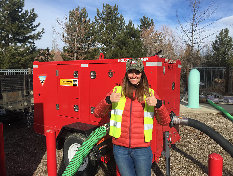 Lydia Peri gives a thumbs up in front of a red water pump