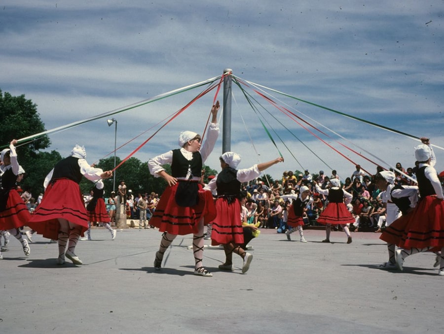 : A group of dancers participating in what appears to be a version of the Zinta Dantza, a ribbon dance. The colored ribbons are braided with the movement of the dancers around the pole. Metaphorically, the dance represents the process of life, the obstacles encountered as life progresses, and the passing from life to the afterlife.